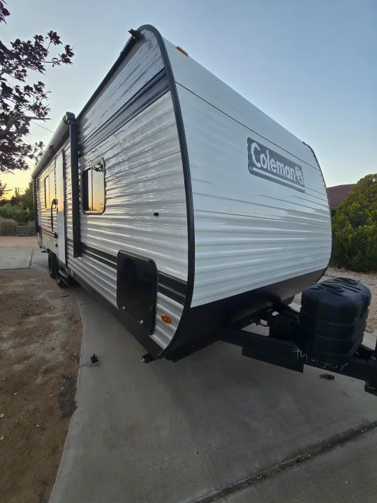 Modern Coleman travel trailer, perfect for an RV rental. Sleek design, parked outdoors with warm light reflection.. Colman 23B 2025