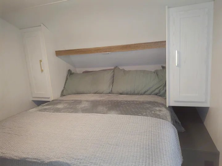 Cozy RV rental bedroom featuring a comfortable bed, overhead shelf, and stylish wall-mounted cabinets for efficient space.. Heartland RVs Eddie Bauer 261BHC 2024