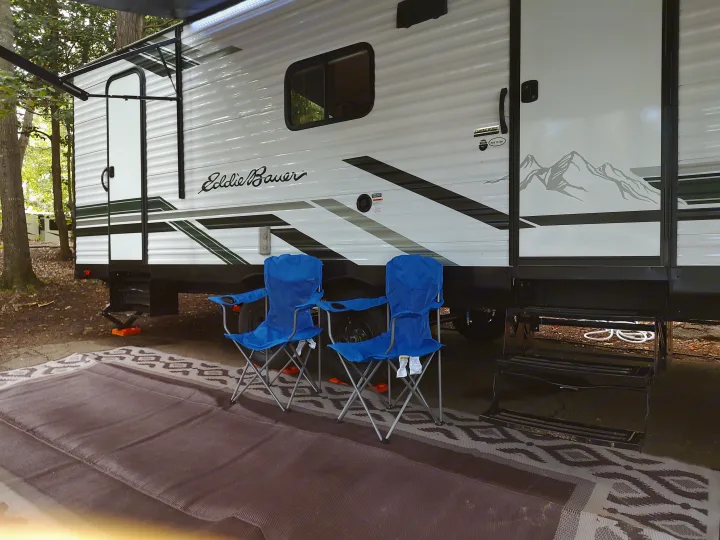 Side view of an Eddie Bauer rv rental at a campsite, showing its awning, outdoor chairs, and mat.. Heartland RVs Eddie Bauer 261BHC 2024