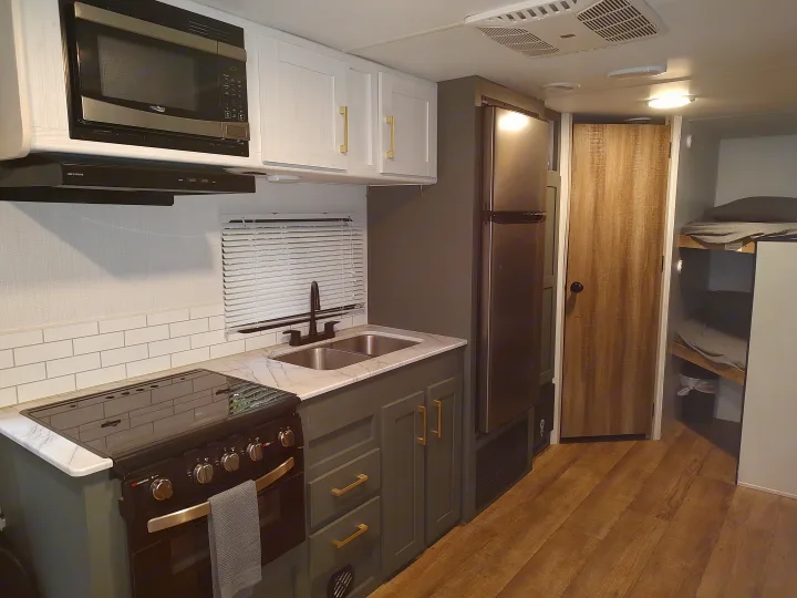 Modern RV rental interior with a fully equipped kitchen, gray cabinets, gold hardware, and cozy bunk beds.. Heartland RVs Eddie Bauer 261BHC 2024