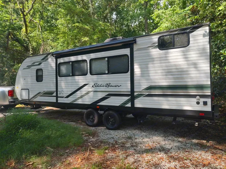 Eddie Bauer travel trailer RV rental, parked on gravel in a shaded campsite, ready for your outdoor adventures.. Heartland RVs Eddie Bauer 261BHC 2024