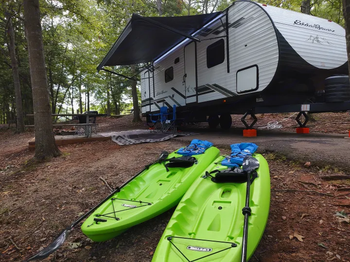 An Eddie Bauer rv rental parked at a serene wooded campsite, ready for adventure with two lime green kayaks and gear.. Heartland RVs Eddie Bauer 261BHC 2024