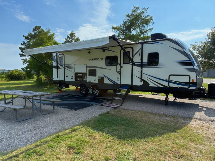 RV rental: White travel trailer with awning and picnic table at a scenic gravel campsite. Water visible nearby.. Keystone RV Passport Grand Touring 2020