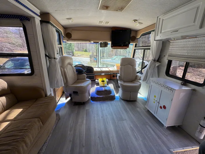 Interior of a bright RV rental: driver's cockpit, passenger seat, sofa, and modern gray flooring.. Fleetwood Southwind 36T 2000