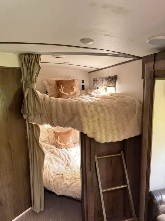 Cozy RV rental features stacked bunk beds with soft cream bedding, antler pillows, and a ladder.. Keystone RV Passport Grand Touring 2020