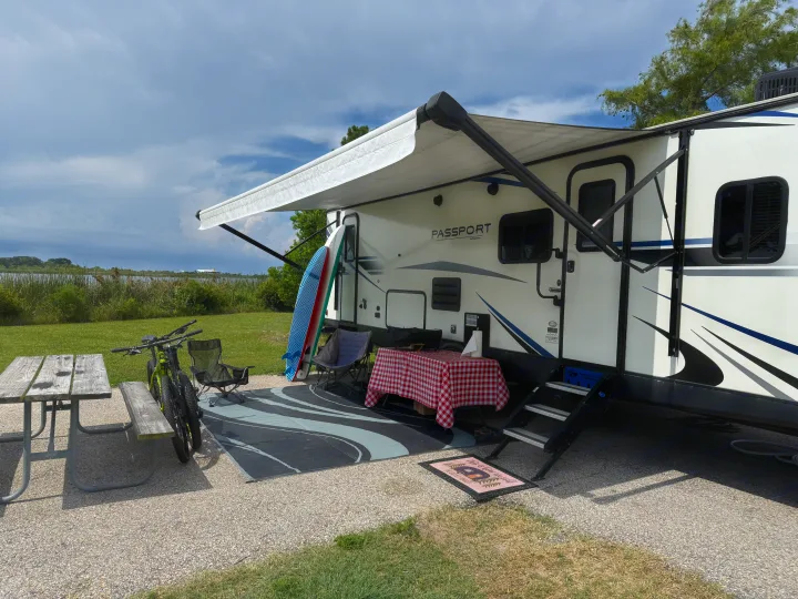 Relaxing RV rental campsite setup: awning, picnic table, bikes, paddleboards, and a lake view.. Keystone RV Passport Grand Touring 2020