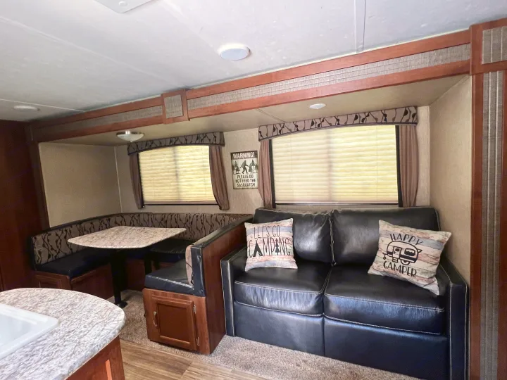 A cozy RV rental interior features a U-shaped dinette, black sofa with camping pillows, and a fun Sasquatch warning sign.. Keystone RV Passport Grand Touring 2017