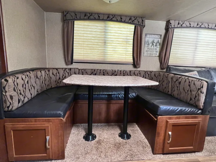 U-shaped dinette in an RV rental, featuring comfortable black leatherette seating, patterned fabric backrests, and a light-colored table.. Keystone RV Passport Grand Touring 2017