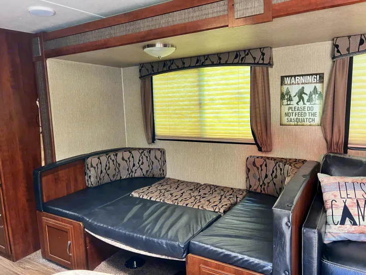 Cozy RV rental interior showing a dinette that converts to a bed, with wood trim, comfy cushions, and a fun Sasquatch sign.. Keystone RV Passport Grand Touring 2017