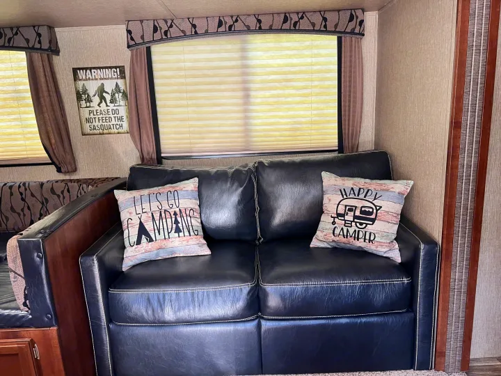 Cozy RV rental interior with black sofa, camping pillows, and a fun sasquatch warning sign.. Keystone RV Passport Grand Touring 2017