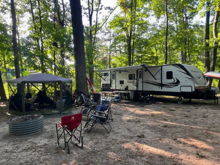 Peaceful RV rental campsite: Passport RV, screen tent, fire pit, chairs, & bikes amidst trees. Your outdoor adventure awaits.. Keystone RV Passport Grand Touring 2017