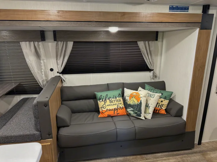 Cozy RV rental interior with a gray sofa, decorative camping pillows, and modern wooden trim.. Forest River Campsite reserve 26CJ 2025