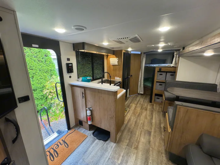 Bright RV rental interior featuring a modern kitchen, dinette, bunk beds, and welcoming open door with outdoor view.. Forest River Campsite reserve 26CJ 2025