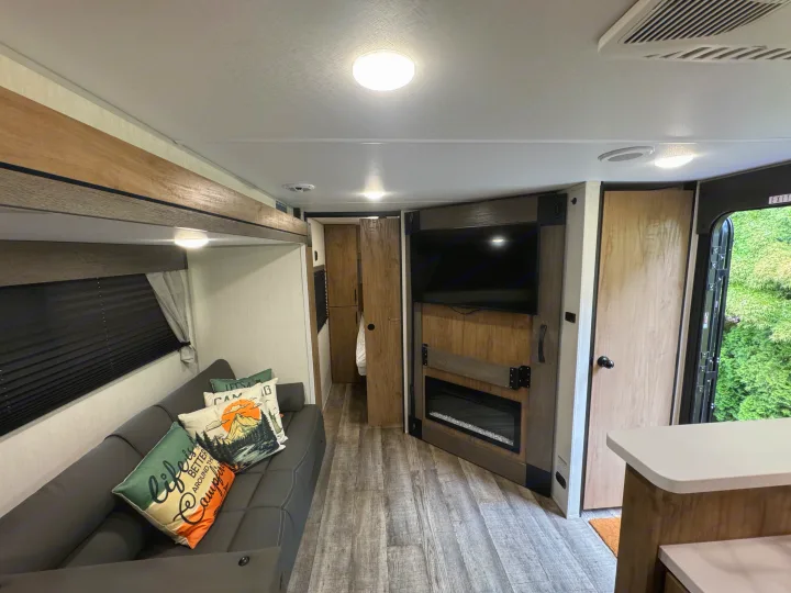 Spacious rv rental interior with a sofa, TV, fireplace, and wood-look flooring. Bright lighting, modern design, ready for adventure.. Forest River Campsite reserve 26CJ 2025
