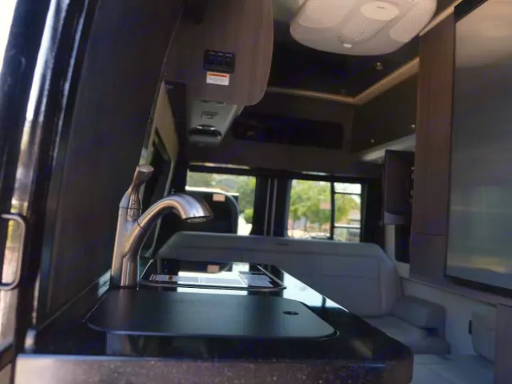 Spacious RV rental interior: view of a dark counter with a shiny faucet/sink, light seating, and a large TV.. Airstream Interstate 2020