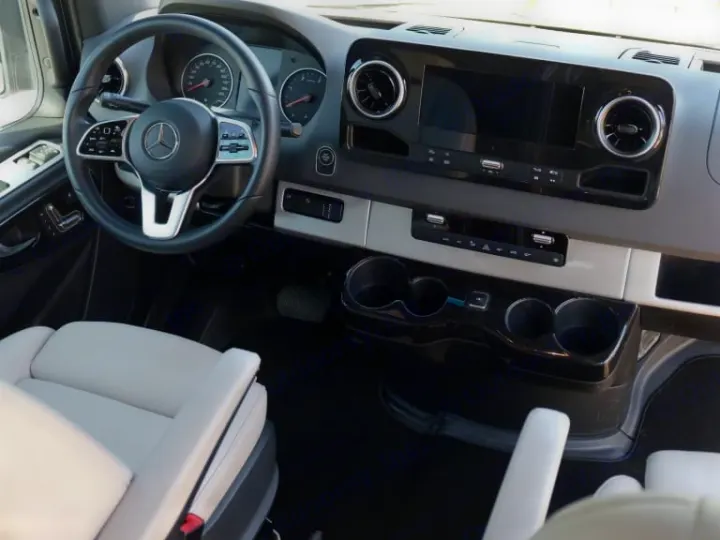 Modern Mercedes-Benz RV rental interior. Driver's cockpit view with detailed dashboard, large screen, and light gray seats.. Airstream Interstate 2020