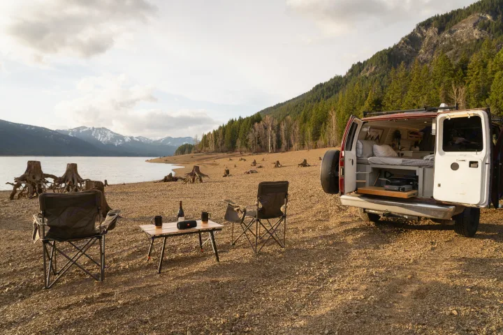 RV rental: Camper van parked on a vast lake shore with mountains. Camping chairs and table set up for relaxation.. Ford Econoline 2006