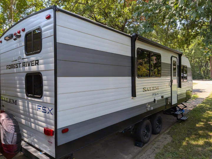 A white and gray Forest River Salem FSX travel trailer, ready for your next RV rental adventure, parked under trees.. Forest River Salem FSX 266BHLE 2025
