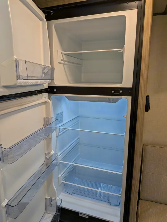 Empty two-door refrigerator, with clear shelves and door bins, open in an RV rental, ready to be stocked.. Forest River Salem FSX 266BHLE 2025