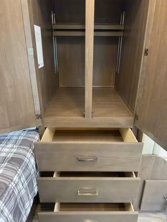 RV rental bedroom storage: open wardrobe with hanging rods & three open drawers next to a bed, showing ample space.. Thor Freedom Elite 2020