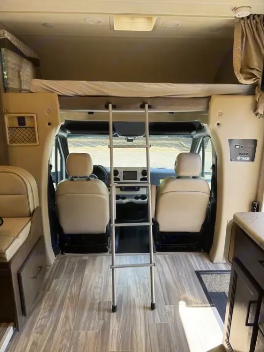 Spacious RV rental interior: cab-over bunk with ladder, front seats, and wood-look flooring. Ready for travel!. Thor Freedom Elite 2020