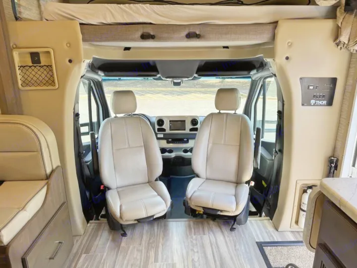 View of an RV rental's front cabin. It shows the two driver/passenger seats, overhead bunk, and part of the living area.. Thor Freedom Elite 2020