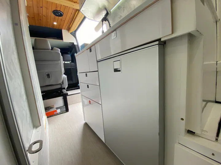 RV rental interior: Sleek white camper van kitchen with fridge, cabinets, and wood ceiling. Ready for your adventure!. Mercedes Sprinter 2500 4x4 2021