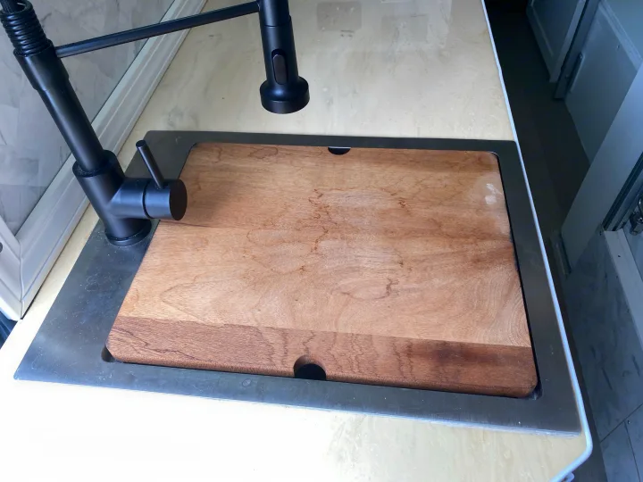 This RV rental kitchen features a sleek black pull-down faucet, a sink, and a wooden cutting board covering the sink on a light counter.. Mercedes Sprinter 2500 4x4 2021