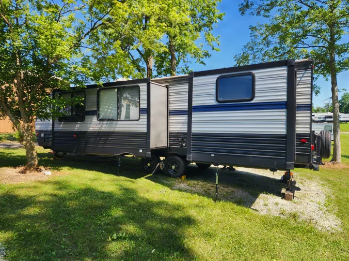 This travel trailer RV rental, set up on a grassy site, awaits your camping trip under blue skies and green trees.. Forest River Cherokee 2019
