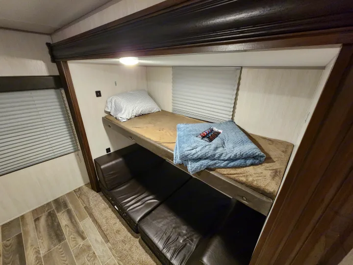 Inside an RV rental: cozy bunk beds with light, window blinds, and lounge space below.. Forest River Cherokee 2019