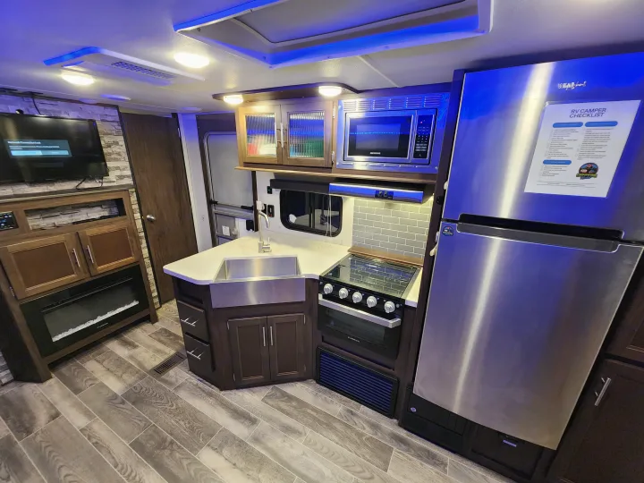 Modern RV rental interior featuring a full kitchen (fridge, stove, microwave, sink), TV, electric fireplace, and blue lighting.. Forest River Cherokee 2019