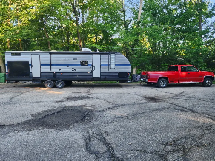 A red pickup truck tows a white & blue travel trailer on asphalt, ready for your next rv rental trip!. Forest River Cherokee 2019