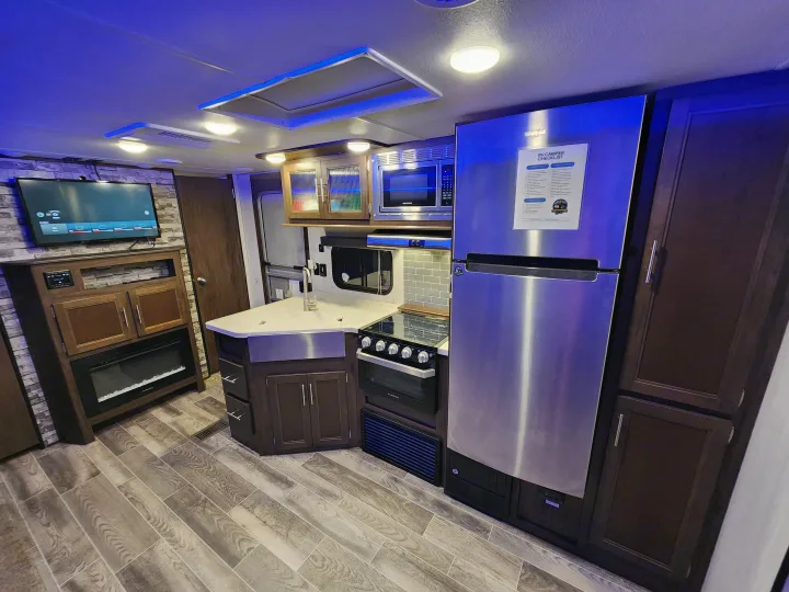 Modern RV rental interior features a kitchen with stainless steel appliances, living area, TV, and fireplace.. Forest River Cherokee 2019