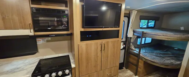 Inside this RV rental: a kitchen with microwave, entertainment center with TV, and cozy bunk beds. Ready for travel.. Grand Design Imagine 2021