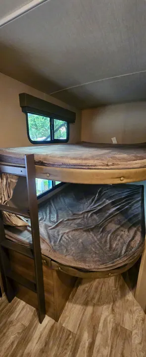 Interior of an RV rental featuring built-in bunk beds, a window with outdoor views, and wood-look flooring.. Grand Design Imagine 2021