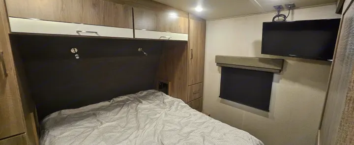 Cozy RV rental bedroom featuring a bed, overhead storage, window, and wall-mounted TV for comfortable travel.. Grand Design Imagine 2021