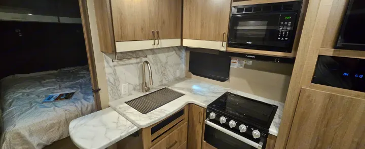 Modern rv rental kitchen area with a sink, microwave, stove, and an adjacent bedroom visible. Compact layout.. Grand Design Imagine 2021
