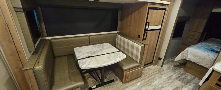 Inside this RV rental: a comfortable dinette with U-shaped booth seating & marble-look table, plus fridge & bedroom access.. Grand Design Imagine 2021