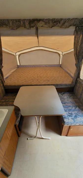 Interior of an RV rental pop-up camper: bed, dining area with table & bench, and small kitchen counter.. Starcraft Starcraft Popup Trailer 2002