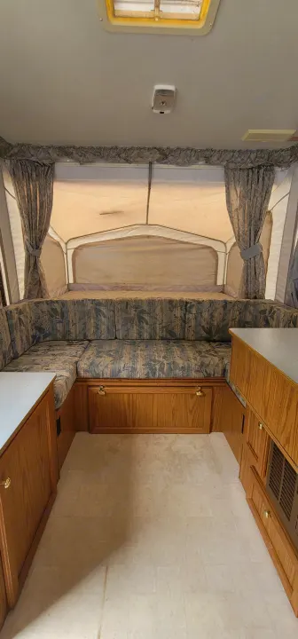 Explore this RV rental interior: a bright, cozy space featuring a U-shaped dinette, patterned cushions, and wood cabinetry.. Starcraft Starcraft Popup Trailer 2002
