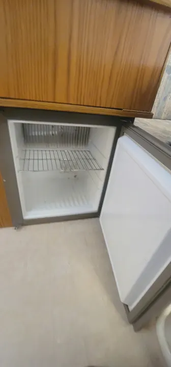 Inside an RV rental, a compact refrigerator is open, revealing empty wire shelves. Ready for your snacks!. Starcraft Starcraft Popup Trailer 2002