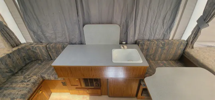 RV rental interior: Functional kitchen counter with sink, dining table, & U-shaped seating.. Starcraft Starcraft Popup Trailer 2002