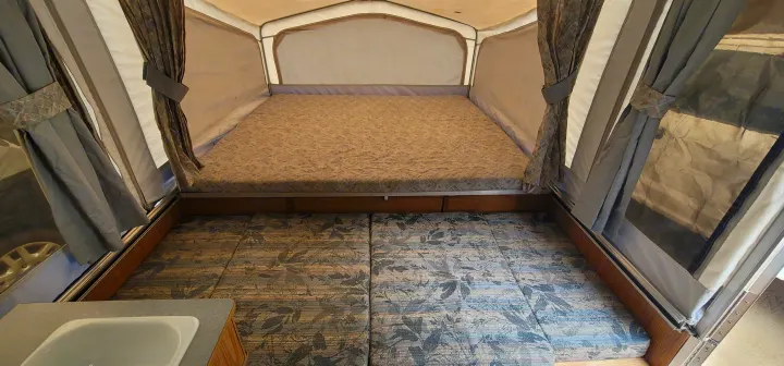 RV rental pop-up camper interior, showing a cozy bed, patterned seating, and a partial sink. Perfect for camping!. Starcraft Starcraft Popup Trailer 2002