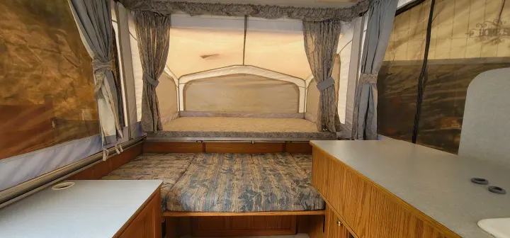 An RV rental's pop-up camper interior with two beds (one raised bunk), curtains, and counter space.. Starcraft Starcraft Popup Trailer 2002
