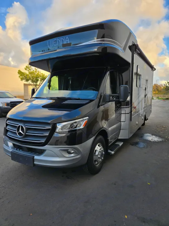 Sleek black & silver Mercedes-Benz Sprinter RV rental, with "Vienna" branding, parked under a cloudy sky. Ready for adventure.. Renegade Custom Coaches Vienna 2021