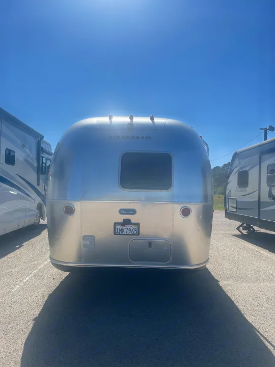 Rear view of a shiny Airstream Bambi travel trailer at an RV rental lot, parked next to other RVs under a clear sky.. Airstream Bambi 2020