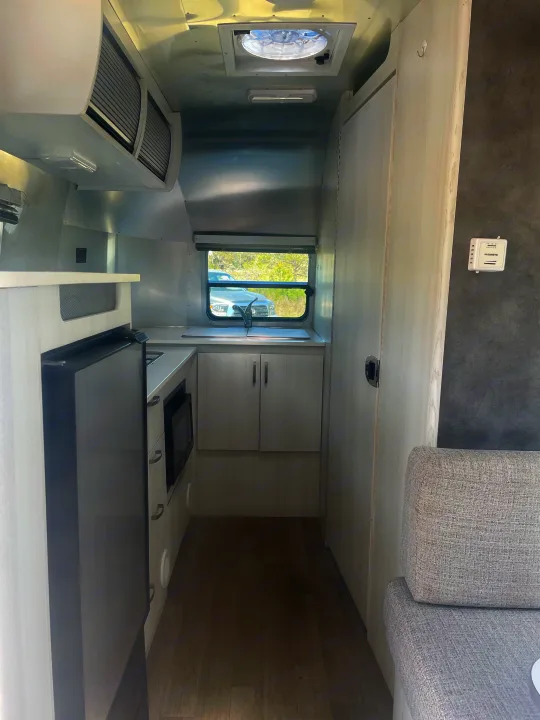This rv rental features a modern, compact galley kitchen with appliances and ample storage, extending to a comfortable living space.. Airstream Bambi 2020