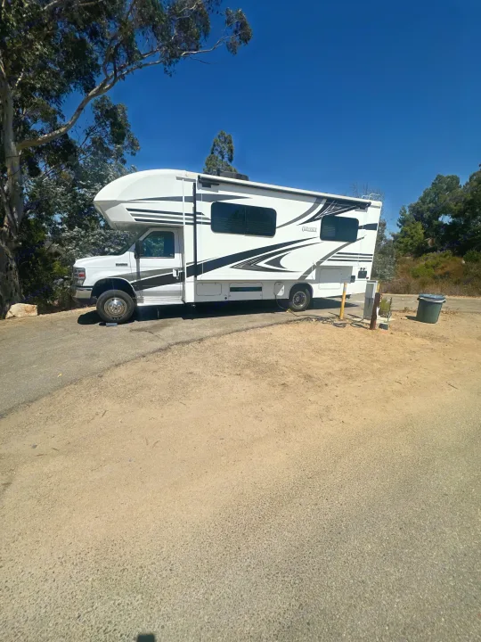 White Class C RV rental (Odyssey) parked at a sunny campsite. Ready for your outdoor adventure!. Entegra Coach Odyssey 2019
