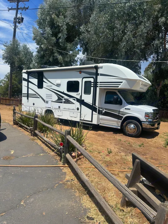 White Class C Entegra Odyssey RV rental parked outdoors, next to a rustic wooden fence on a sunny day.. Entegra Coach Odyssey 2019