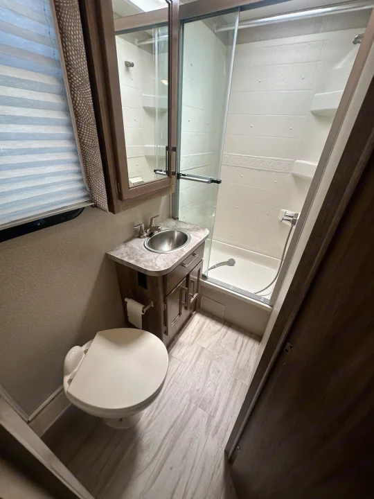 This RV rental features a clean, compact bathroom with a toilet, vanity sink, and glass-door shower, ideal for travel comfort.. Entegra Coach Odyssey 2019